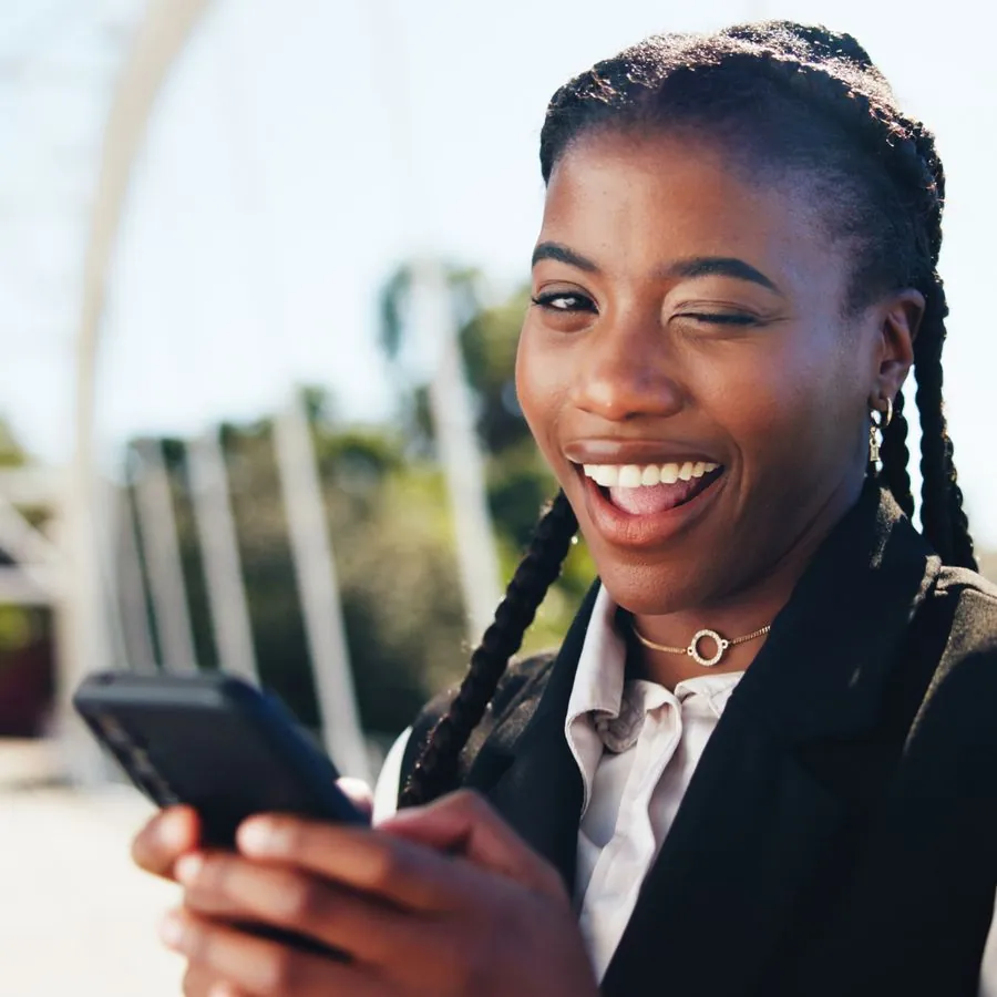 Mulher sorrindo enquanto olha o celular na rua